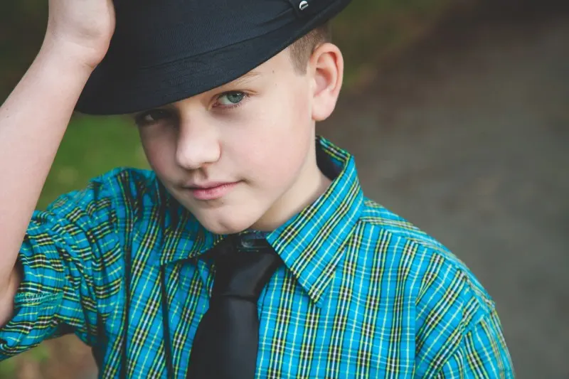 boy in a check shirt and tie tipping a black hat