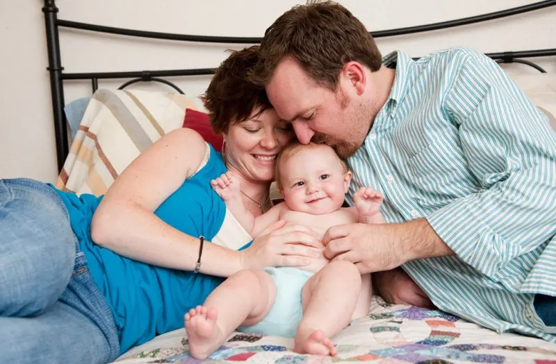 parents cradling their baby on a bed