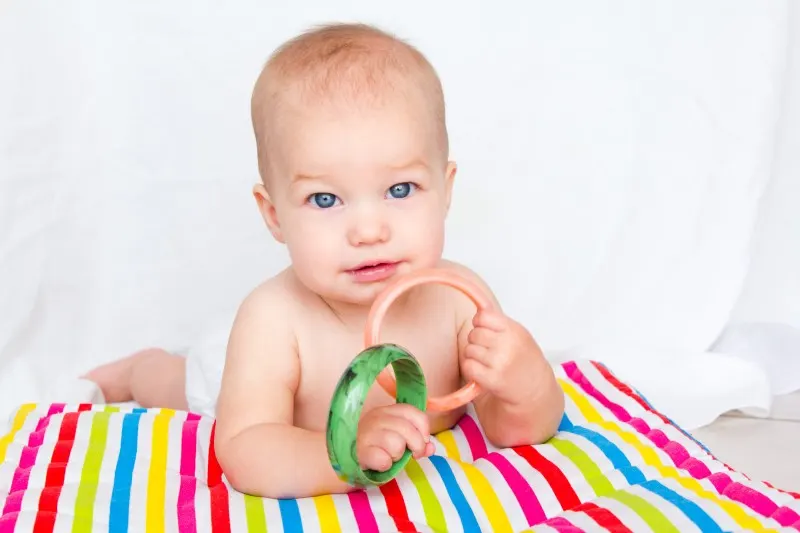 baby on a colorful striped blanket playing with ring toys