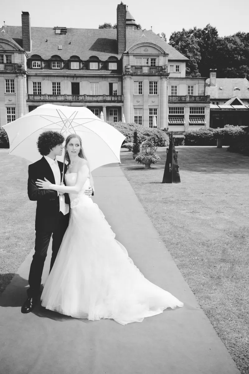 destination germany wedding, couple under a white umbrella in front of a manor, black and white