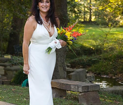 Smiling bride in a white strapless gown holding a colorful spring bouquet outdoors