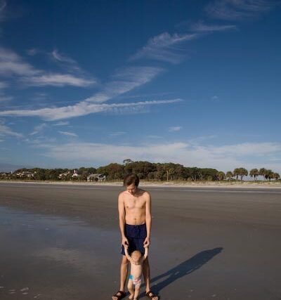 Father walking with his small child on a wide sunny beach