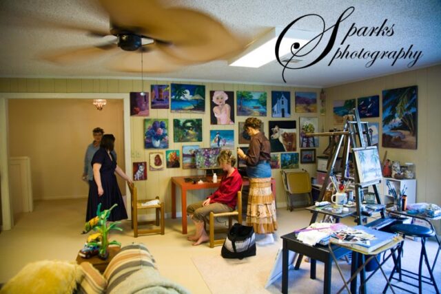 Art studio with floral canvases and two people seated at a work table