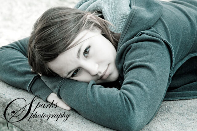 Teenage girl in a green hoodie resting her head on her arm