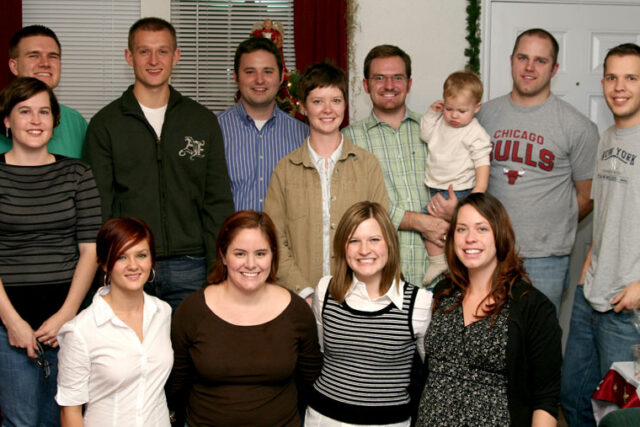 Large family group posing in holiday sweaters at a Christmas party around a baby on the hearth