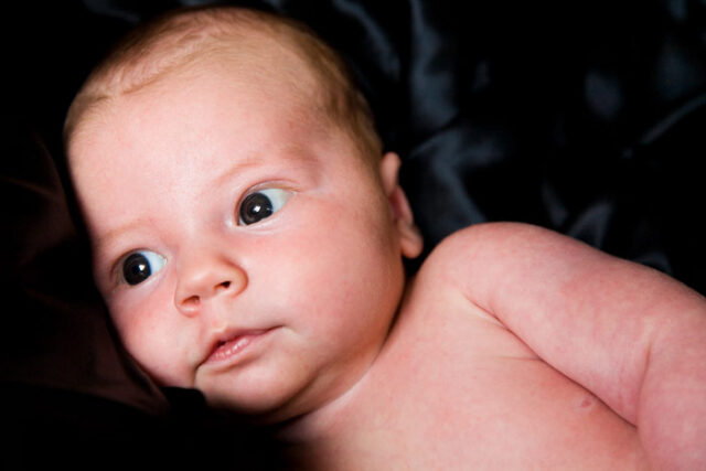 Sleepy newborn head resting on a black satin pillow, color portrait