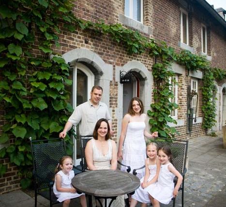 Family gathered around a small round table in front of an ivy-covered brick house