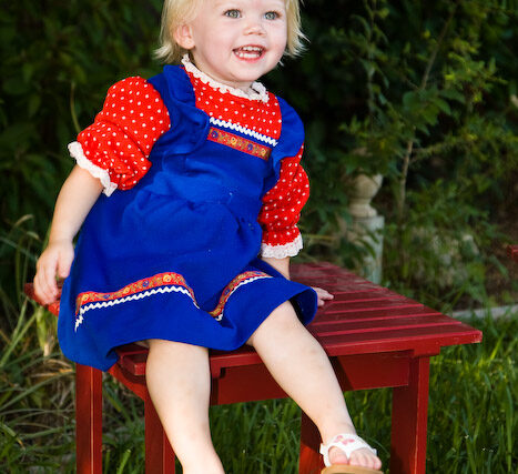 Little girl in red and blue standing by a red bench, laughing