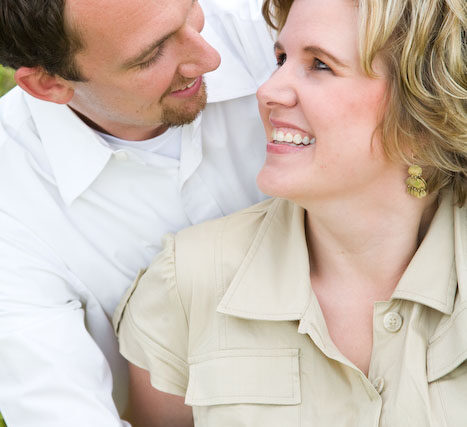 Smiling couple seated close together in the grass looking aside