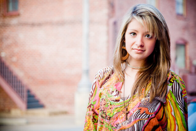 Portrait of a young woman in a colorful top in front of a brick building, color graded