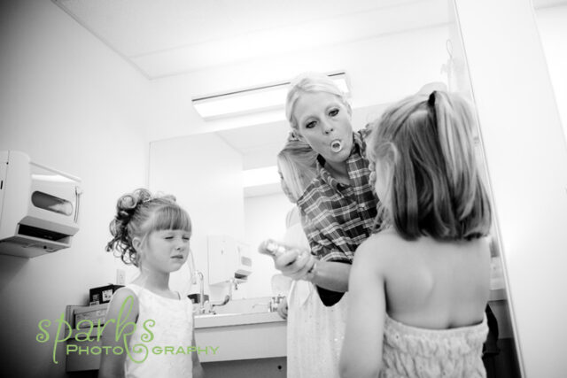 Bride having her hair done while a little flower girl in white sits at the makeup mirror