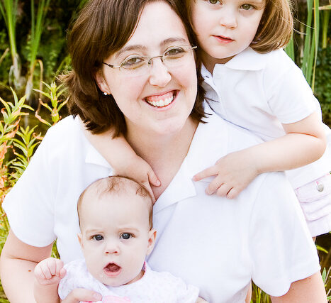 Young mother with her toddler daughter holding the newborn baby brother in a family portrait