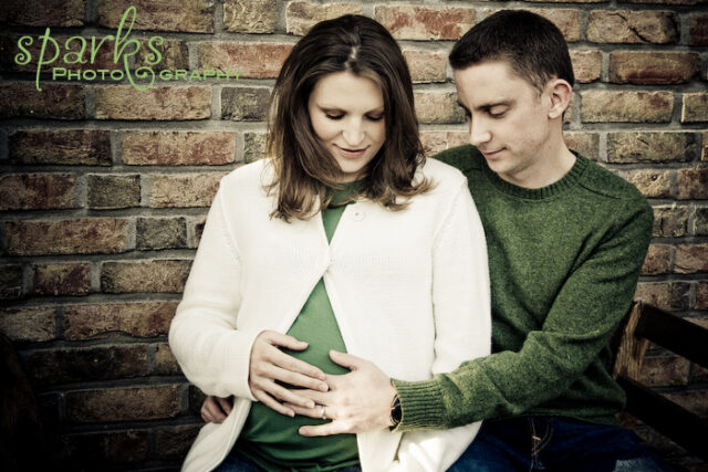 Man in a green polo kissing his pregnant partner's belly while she looks down smiling, black and white