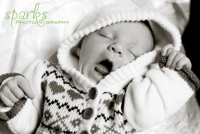 Yawning newborn wearing a cow-print knitted hoodie, black and white