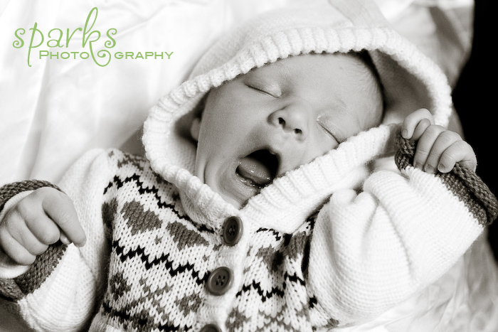 Yawning newborn wearing a cow-print knitted hoodie, black and white