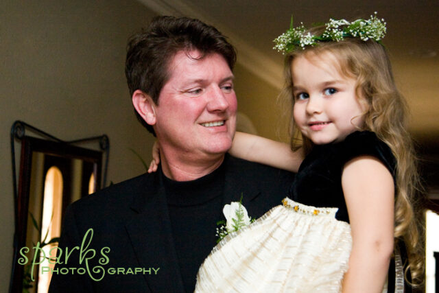 Father and his young daughter in a white dress and flower crown dancing together, smiling