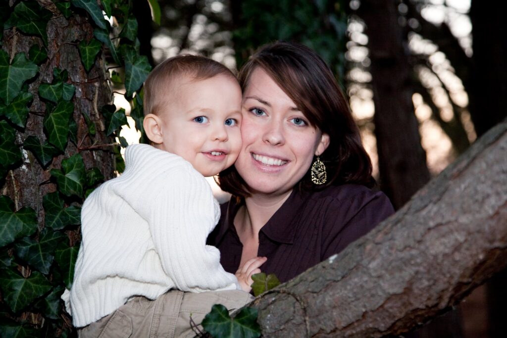 Mother and her smiling toddler son perched together on a tree branch in front of an ivy trellis