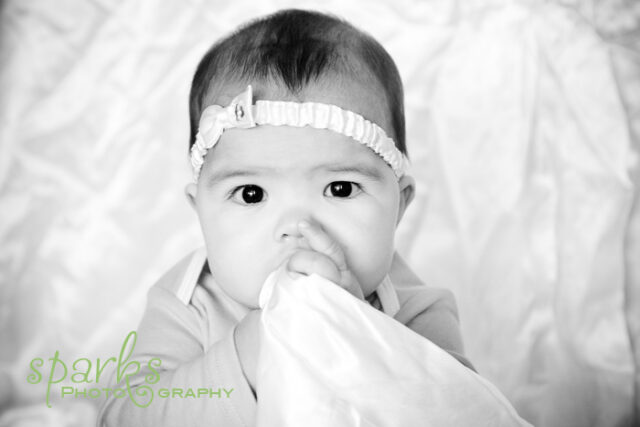 Laughing baby in a white textured gown held up by his mother in a strapless dress