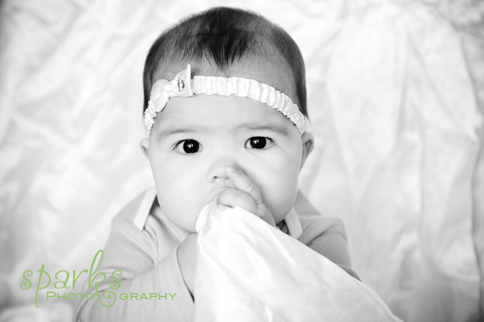 Laughing baby in a white textured gown held up by his mother in a strapless dress