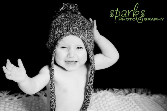 Laughing baby wearing a slouchy knit hat waving both arms, black and white