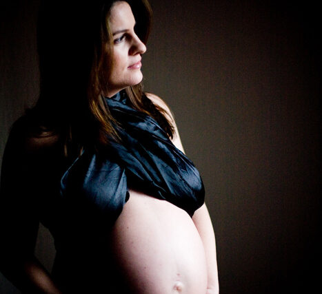 Dramatic maternity portrait of a woman in black satin cradling her pregnant belly in side profile