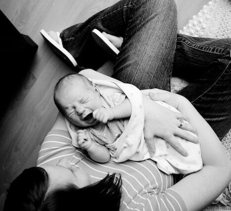 Overhead black and white portrait of a reclining mother holding her newborn on a wooden floor