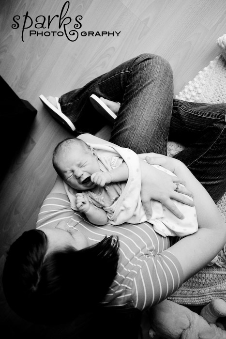 Overhead black and white portrait of a reclining mother holding her newborn on a wooden floor