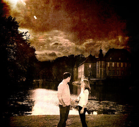 Couple standing on a lake shore at night watching fireworks burst over the water