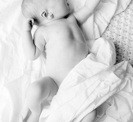 Overhead black and white portrait of a reclining mother holding her newborn on a wooden floor