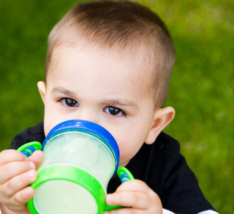 Close-up of a toddler drinking from a green sippy cup while sitting on the grass