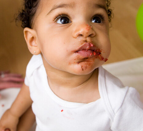 Close-up of a happy toddler with cake on her face after smashing her birthday cake