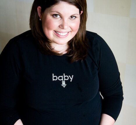 Smiling pregnant woman in a black baby lettering tee cradling her belly