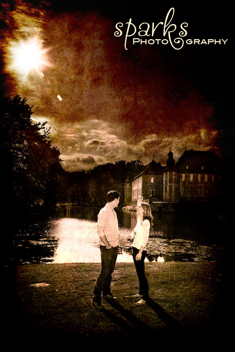 Couple standing on a lake shore at night watching fireworks burst over the water