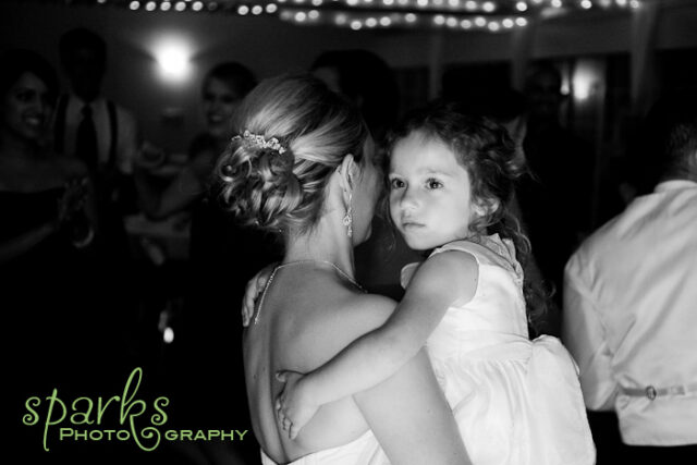 Flower girl hugging the bride from behind at the reception, black and white