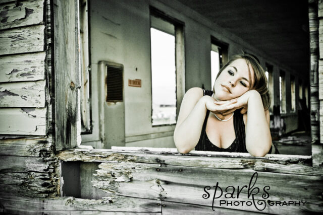Young woman resting her chin on her arms while peering through a broken wooden wall, selective color
