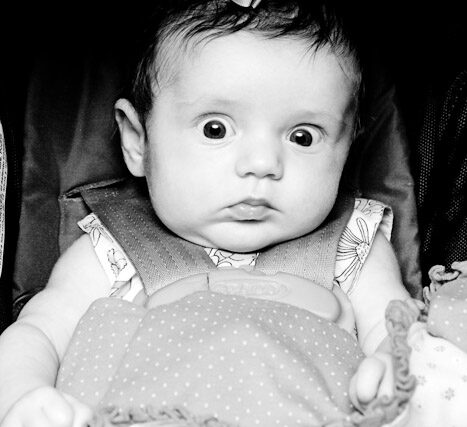 Black and white close-up portrait of a newborn baby wrapped in a knit gown with a ruffled bonnet