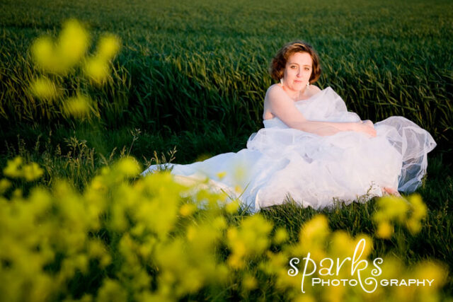 Redheaded bride in a white gown seated in a field of yellow wildflowers