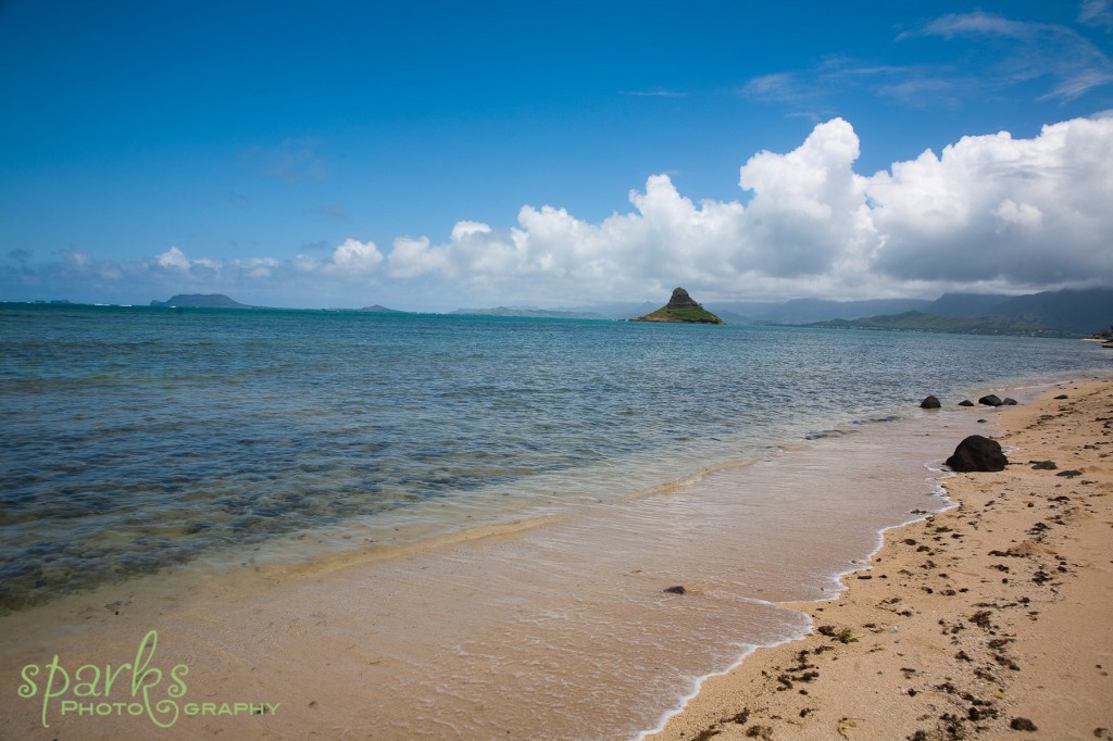 Tropical beach at sunrise with soft clouds, blue sea and a small islet on the horizon