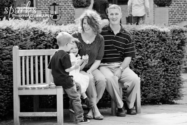 The Wilcox family sits together on a wooden bench in front of a trimmed hedge.