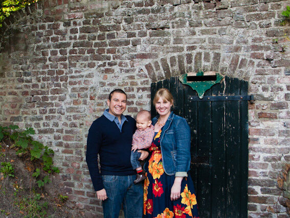 The Hernandez family poses in front of an old stone wall with children peeking over the top.
