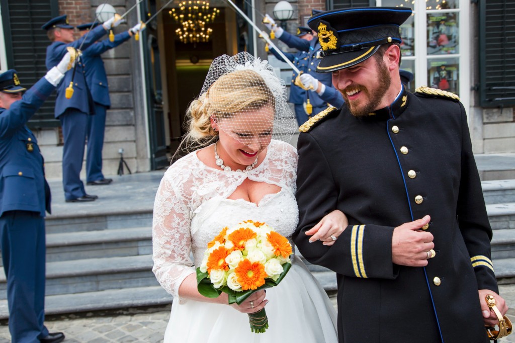 The wedding couple shares a joyful laugh as a military honor guard forms a sword arch behind them.