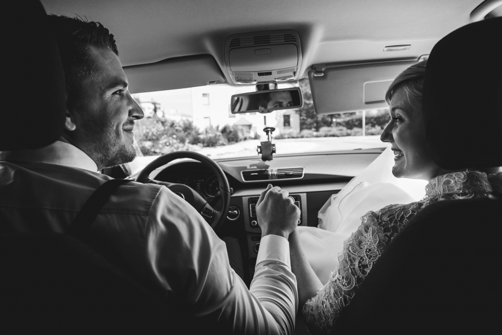 Bride and groom holding hands and smiling at each other inside their car during a Blackforest wedding.