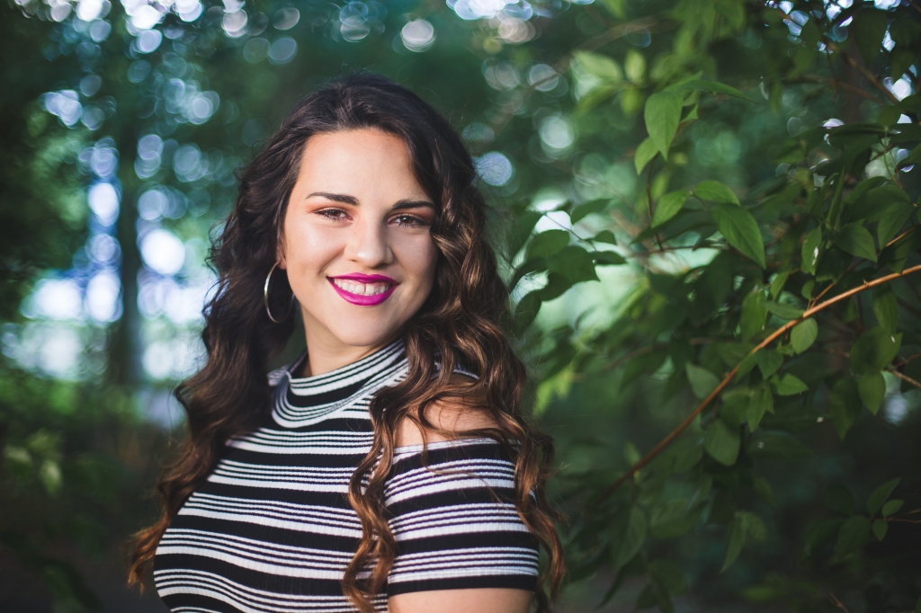 Rachel smiles at the camera during her senior session surrounded by green trees in Brunssum.