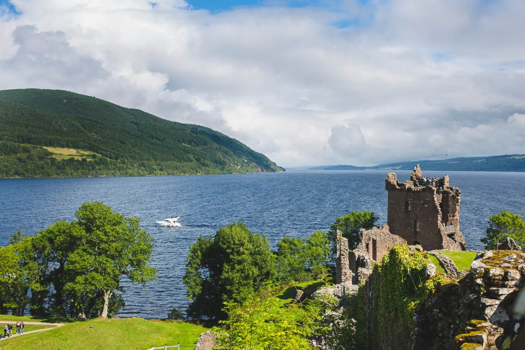 A ruined stone castle overlooks a calm loch framed by green hills in Scotland.
