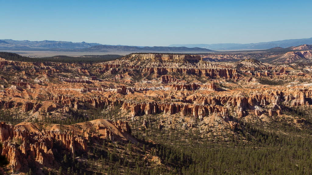 Panorama of the Bryce Canyon National Park amphitheater with hoodoos beneath a clear blue sky and distant mesas