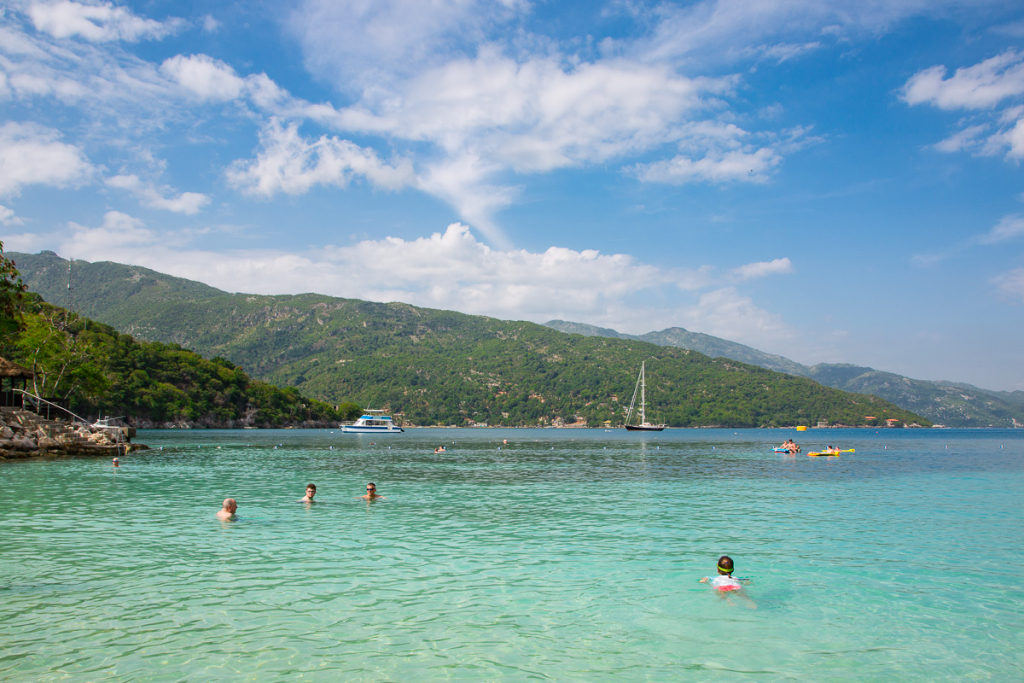 Swimmers in a turquoise lagoon in Labadee Haiti with green mountains and a sailboat in the distance