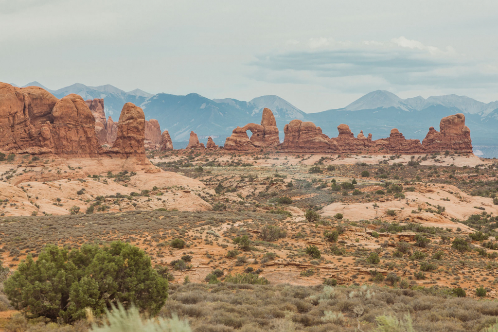 Red rock arches of Arches National Park above a sagebrush desert with distant mountains
