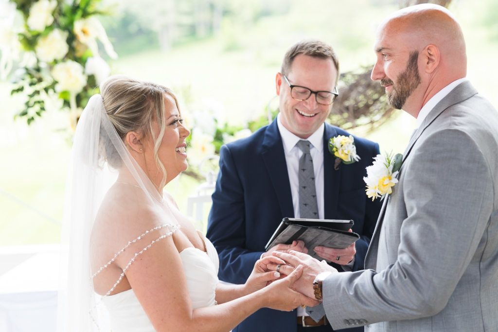 Bride and groom hold hands during their outdoor wedding ceremony as the officiant reads from a tablet