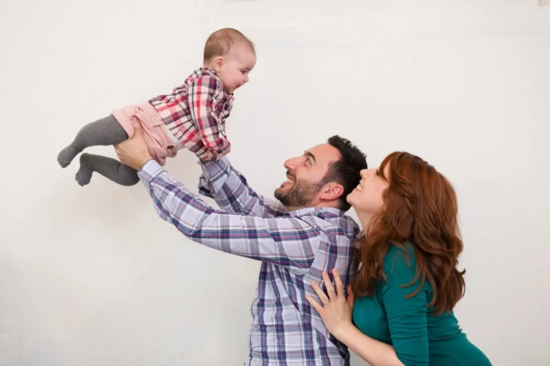 father lifting a laughing toddler as mother looks on