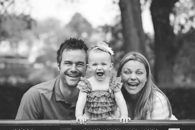 smiling family of three with a toddler on a railing, black and white